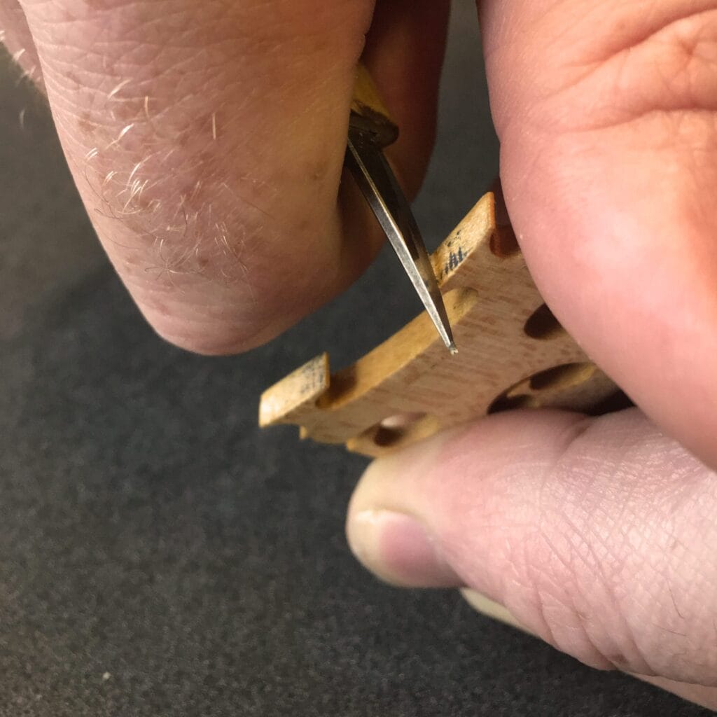 Professional Luthier precision-fitting a violin bridge for optimal string height and tonal clarity.